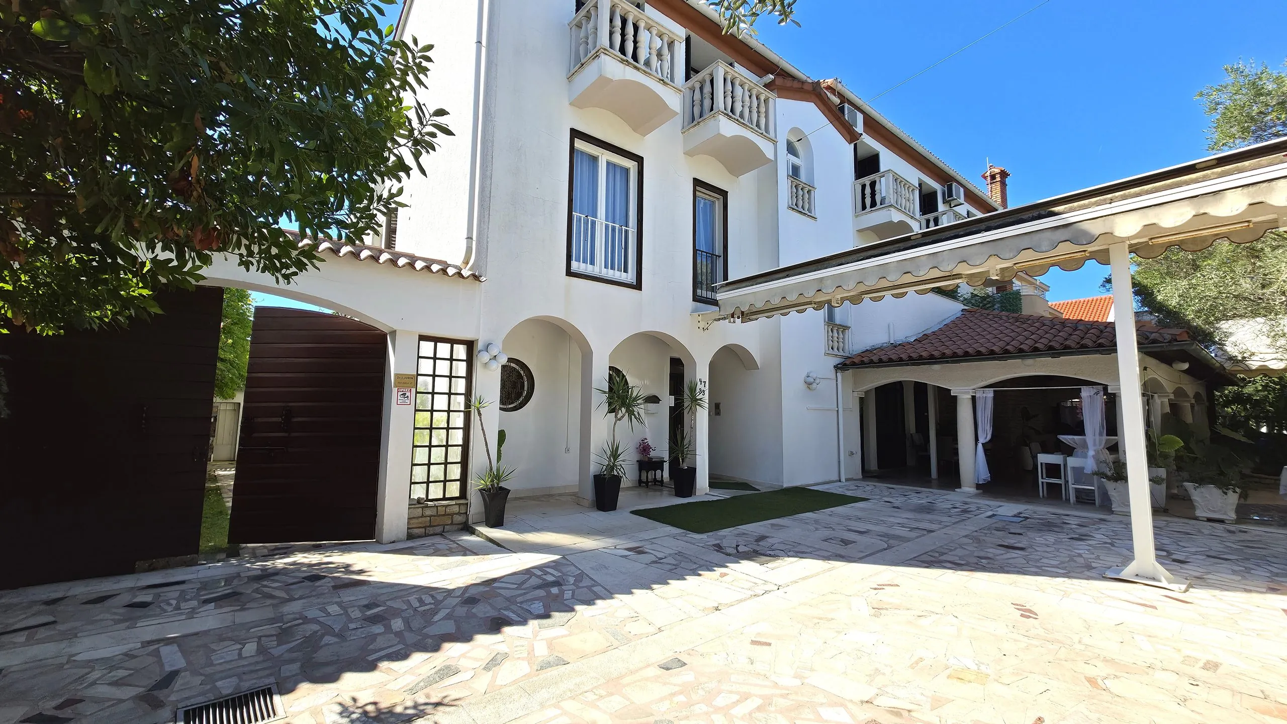White house with balconies, a covered terrace and a paved courtyard