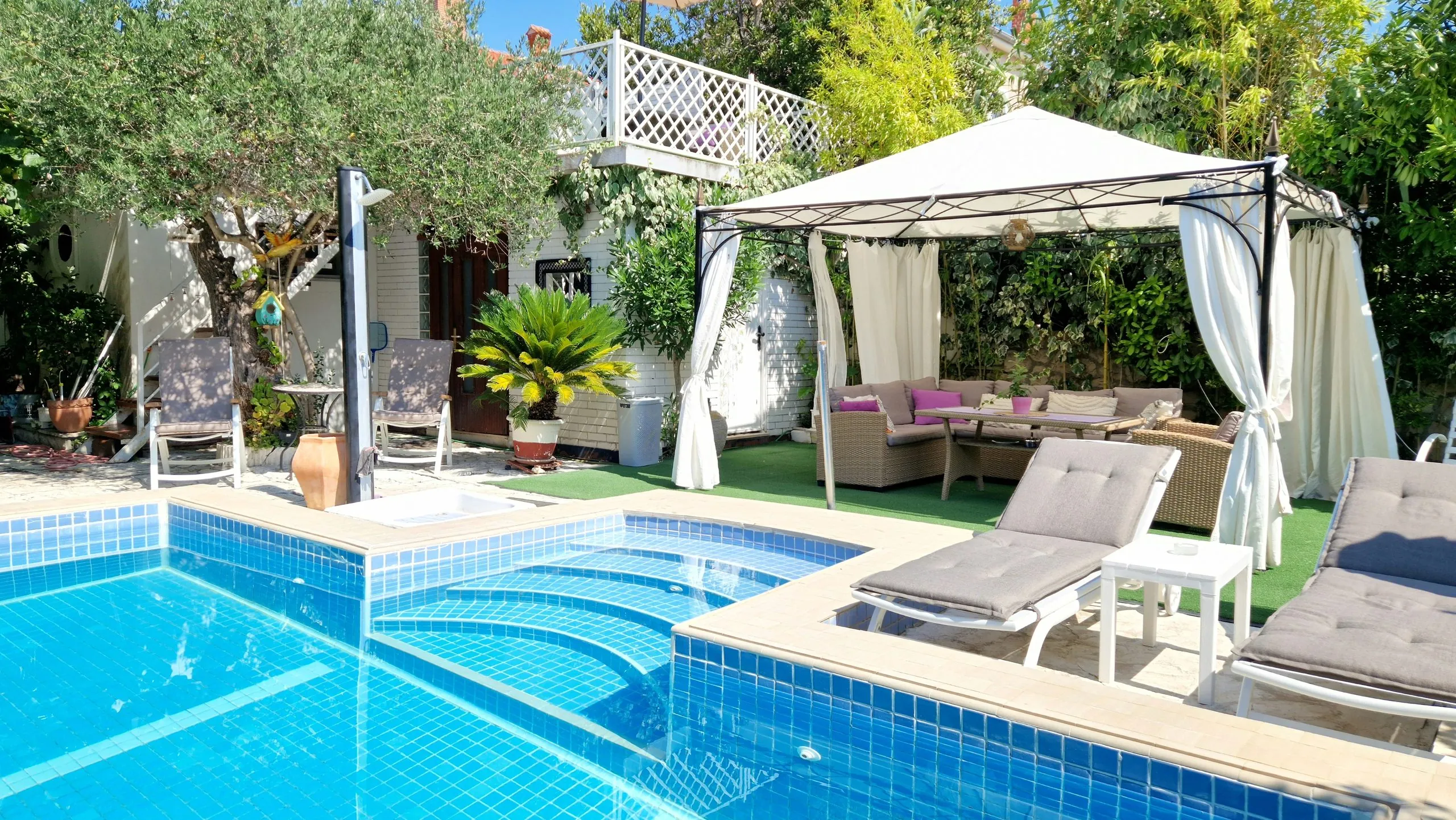 Pool with steps, sun loungers and a gazebo with outdoor seating
